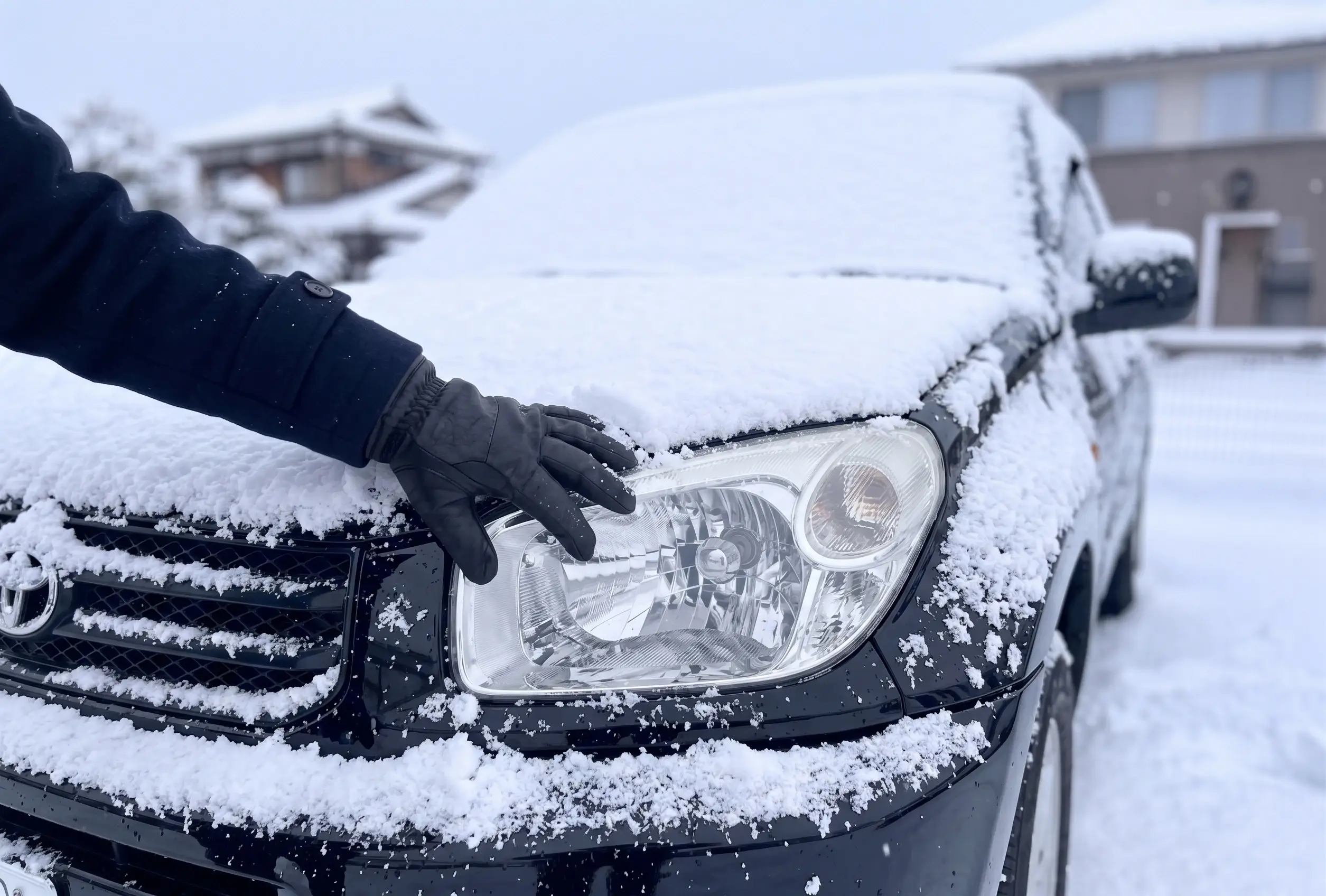 雪の積もった車のライト部分の雪を取り除いてる様子